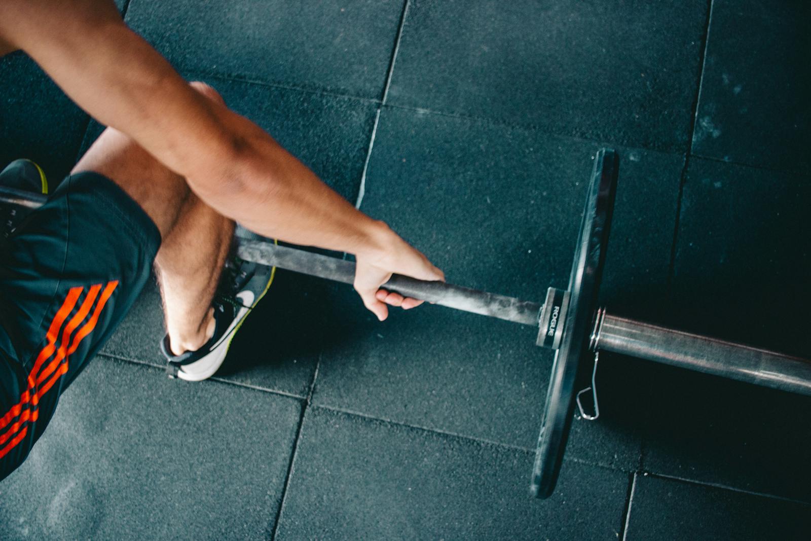 Close-up of an athletic man lifting a barbell in a gym setting, focusing on strength and fitness.